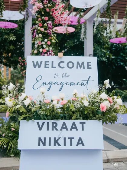 A simple and chic welcome sign for an engagement, nestled in a bed of white and pink flowers, greeting guests as they arrive.
