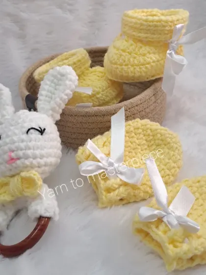 A bright and cheerful baby gift hamper in yellow and white. The set includes booties, mittens, and a bunny rattle, all tied with delicate white ribbons.