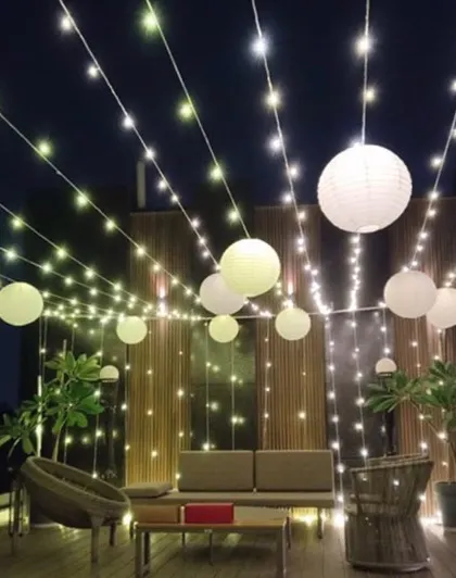 A beautiful terrace setup for a New Year's party, perfect for any evening celebration. The space is decorated with strings of fairy lights and hanging white paper lanterns, creating a warm and inviting atmosphere.