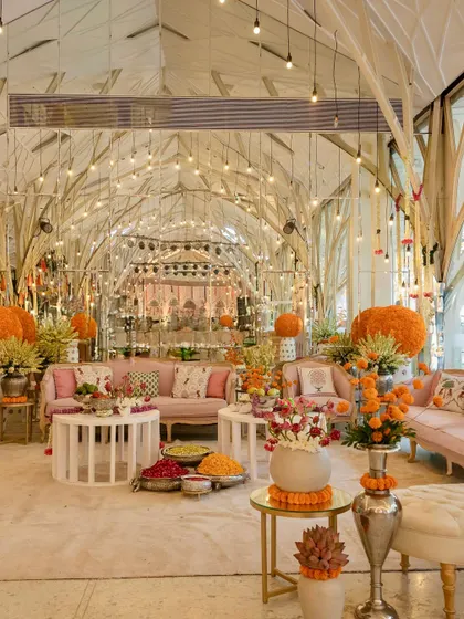A beautiful indoor Mehendi setup, transforming the space with pastel lounges, marigold accents, and traditional garlands for a "pooja to party" vibe.