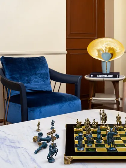 A detail shot of a living corner with a chess set on a marble table and a plush blue velvet chair, illustrating how we layer details to give a space soul.