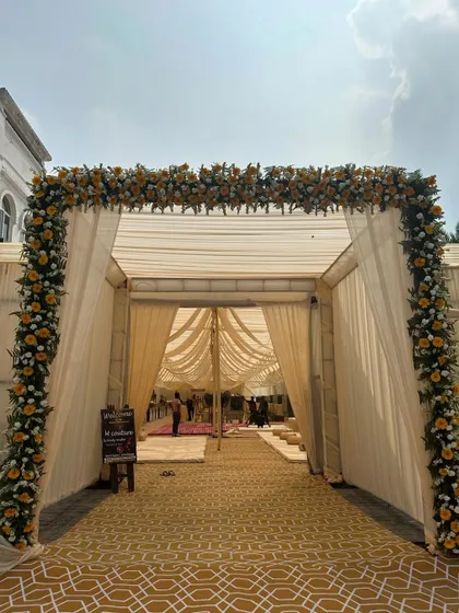 A grand entrance sets the tone for the entire event. We designed this welcoming floral archway for a large religious gathering, using a mix of yellow and white flowers to create an elegant and inviting passage for guests into the beautifully draped tent.