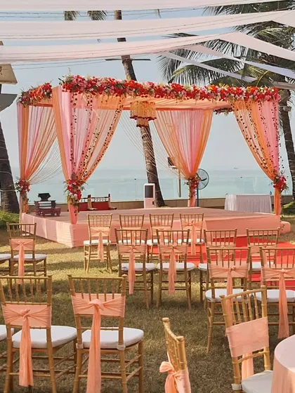 A beautiful peach-themed wedding ceremony on a lawn overlooking the ocean. The decor is light and elegant, with matching chair ties and a floral mandap that perfectly complements the seaside setting.