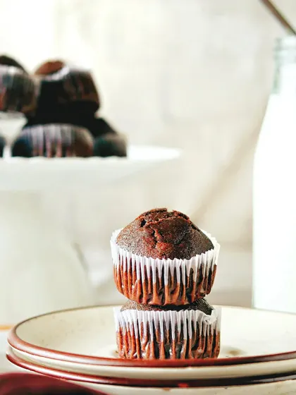 A wider shot of the stacked chocolate muffins, with more muffins on a stand in the background. This composition is great for showing a larger batch of baked goods.