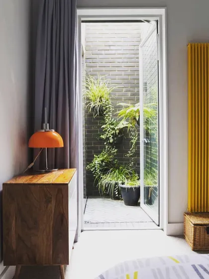 This design shows how even the smallest light well or side yard can become a green feature. Viewed from the bedroom, this narrow space is transformed with a brick wall and climbing plants, bringing nature right to the window.