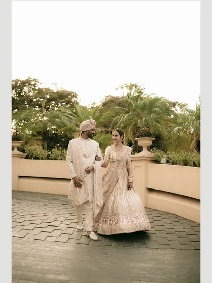 A classic walking shot, capturing the couple's elegance and the beautiful flow of the bride's lehenga.