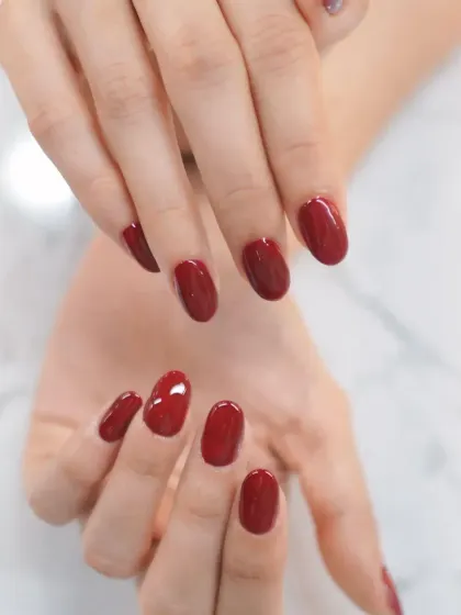 A sophisticated deep red gel polish on perfectly shaped short, natural nails for an elegant and understated look.