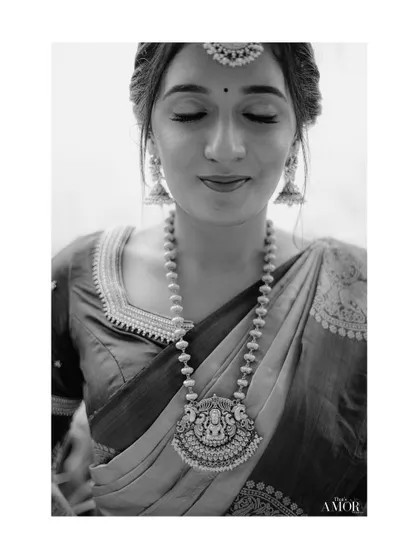 A peaceful black and white portrait of the bride with her eyes closed. The focus is on her calm expression and the stunning temple necklace, creating a moment of quiet beauty.