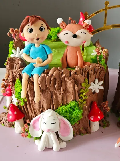 A close-up of the woodland cake, showing the detail on the hand-sculpted boy, fox, and bunny figurines. The tree stump effect is created with textured chocolate buttercream.