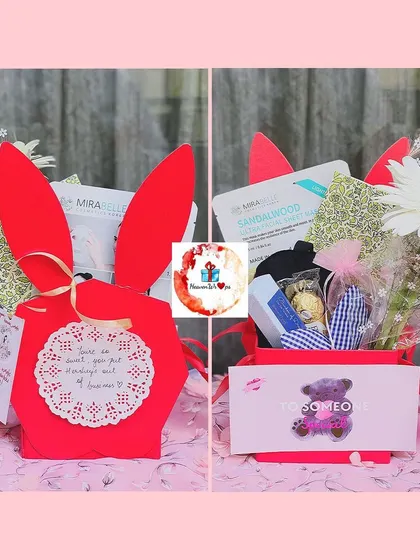A cute bunny-themed gift box in red, filled with a small bouquet of flowers, skincare masks, and other treats for that special someone.