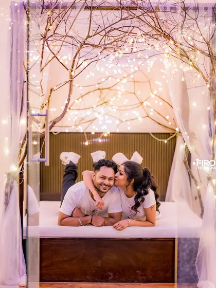 A playful and intimate moment on a bed decorated with fairy-lit branches. This setup is perfect for couples looking for a fun and romantic indoor pre-wedding shoot.
