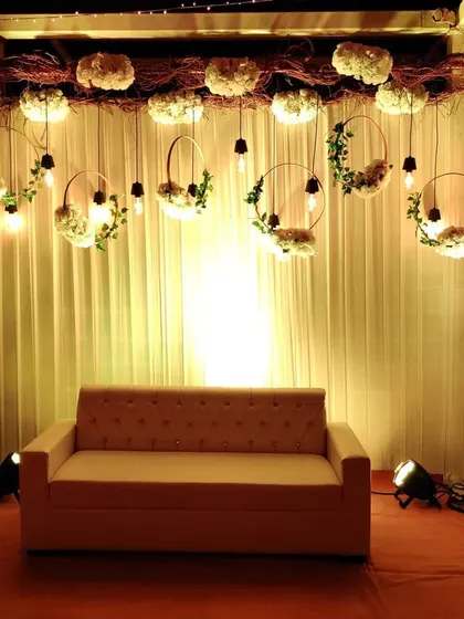 A simple and elegant stage for an engagement party. We used a backdrop of white curtains with hanging floral wreaths and Edison bulbs for a chic and modern rustic look.