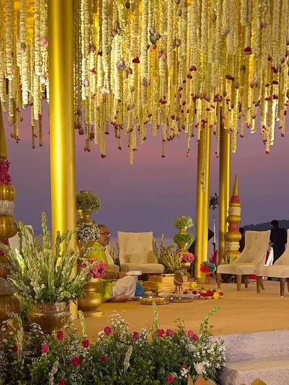 A close-up of the mandap seating, showing the intricate floral hangings and the stunning view of the sea at dusk.