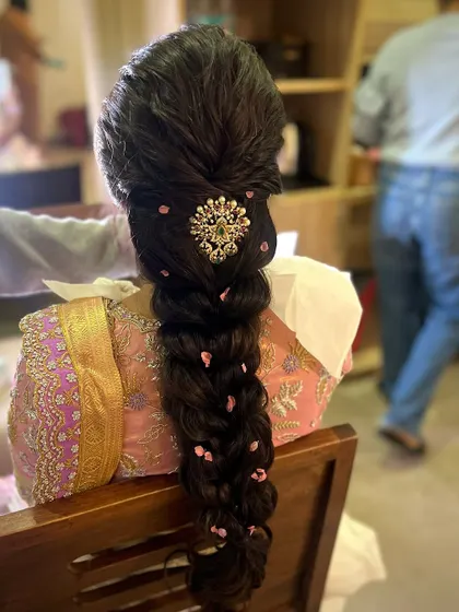 A behind-the-scenes shot of the modern braid being styled. The small pink floral details add a soft, romantic touch to the overall look.