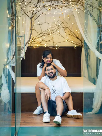 A playful and cozy indoor shot with the couple relaxing in a room decorated with fairy lights.