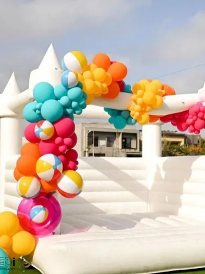 A white bouncy castle decorated with a colorful balloon garland. This is a chic and modern take on a classic party favorite, perfect for stylish kids' birthdays.