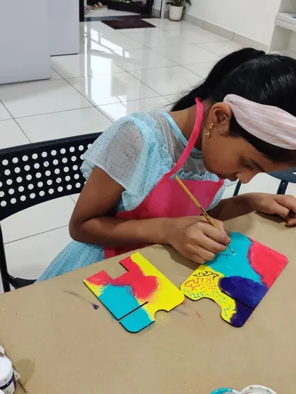 A young artist in a pink apron carefully adds details to her colorful desk calendar puzzle piece.