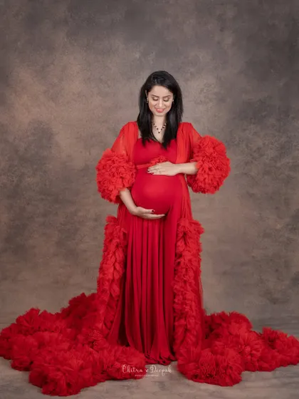 A quiet moment of reflection. This full-length portrait in a dramatic red gown captures the peaceful anticipation of motherhood.