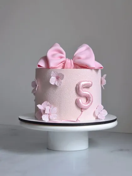 A dreamy pink bow cake for a 5th birthday. This design combines a soft velvet texture, a balloon number, and a perfectly tied bow for a sweet and modern look.