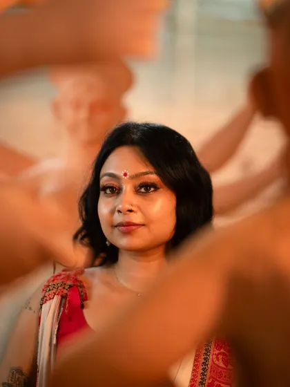 A creative, framed shot showing the model's face among the idols. The focus is on her expressive eyes, enhanced with kohl and a traditional bindi.