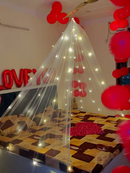 A simple and sweet romantic room decoration. The bed is decorated with a fairy light canopy, and the room is filled with red balloons and 'I LOVE YOU' foil letters.