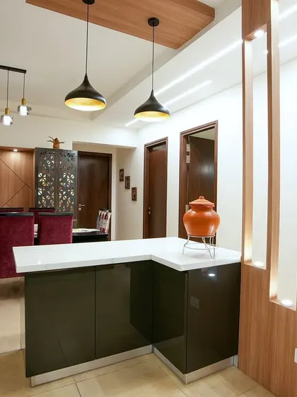 This dining area for Palak and Ashwani features rich wood tones, a breakfast counter with pendant lights, and a formal dining setup with plush red chairs, creating multiple zones for eating and entertaining.