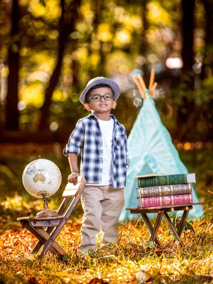 A young boy dressed as an explorer stands in a field with a globe and books. The warm, golden light of the outdoors adds a beautiful touch to this adventurous themed portrait.