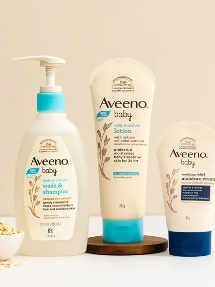 A clean and gentle product grouping for Aveeno Baby. The composition uses natural ingredients like oats and wheat against a soft, neutral background to emphasize the product's natural and soothing qualities.