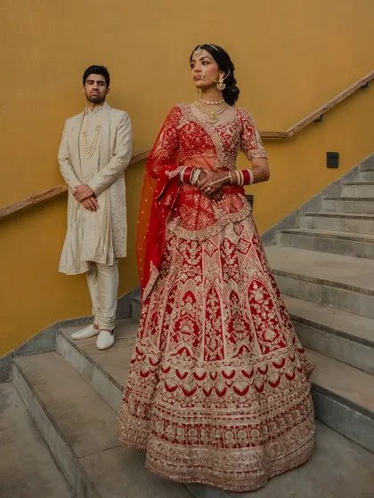 A regal portrait of the couple in their stunning red and cream wedding attire. We use architectural elements like staircases to add a touch of grandeur to our compositions.