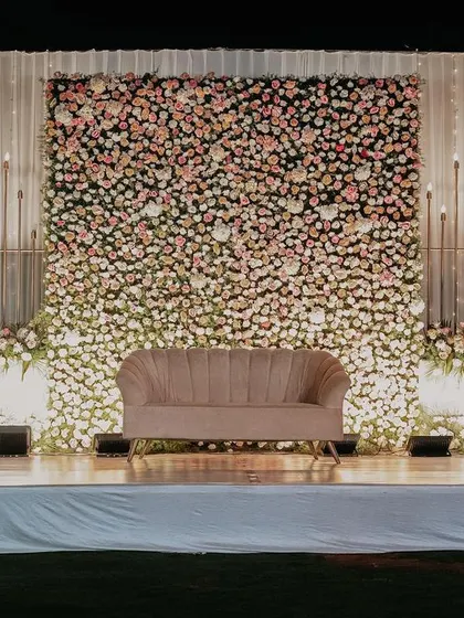 An elegant engagement stage featuring a massive wall of pastel pink and white flowers, creating a soft and romantic backdrop.