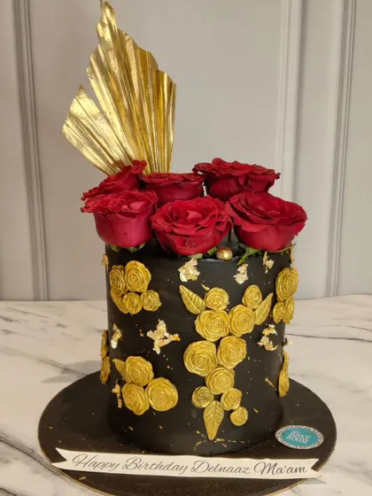 A glamorous black and gold cake for actress Delnaaz Irani's birthday. The cake is decorated with golden roses and topped with fresh red roses for a touch of drama and elegance.