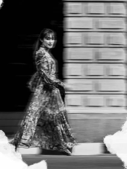 An artistic shot using motion blur to create a dreamy, ethereal effect. This black and white photo has a beautiful, ghostly quality as she walks past a heritage building.