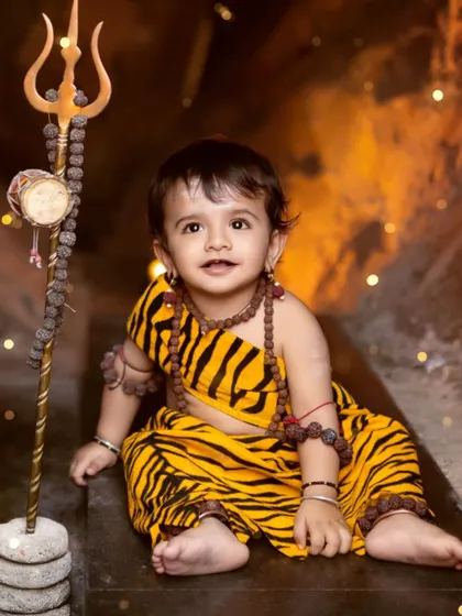 A sweet portrait of a toddler dressed as Lord Shiva, sitting in our cave setup with his trishul.