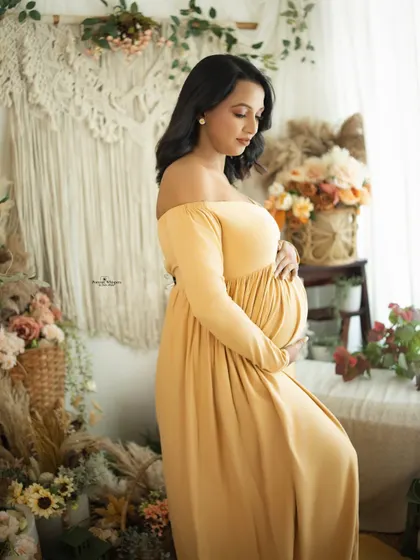 A side-profile portrait by the window, using soft natural light. The mother-to-be looks down at her bump in a moment of quiet connection.