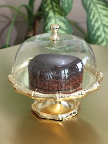The classic Gold Cloche stand with a bamboo-style base, holding a rich chocolate cake. Its timeless design is perfect for any occasion, from birthdays to holiday gatherings.