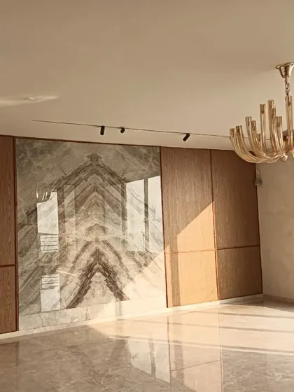 This penthouse living room is nearing completion, and the key elements are already shining. The feature wall combines bookmatched marble with warm wood paneling, creating a luxurious and symmetrical focal point. Natural light from the large window illuminates the polished marble floors, enhancing the sense of space and elegance.
