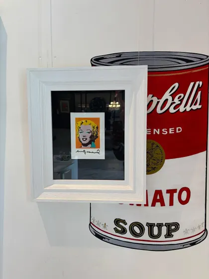 A signed 'Postcard Marilyn' by Andy Warhol, displayed against a giant Campbell's soup can graphic. This is one of the most important artworks of the 20th century and a pioneering piece of pop art.