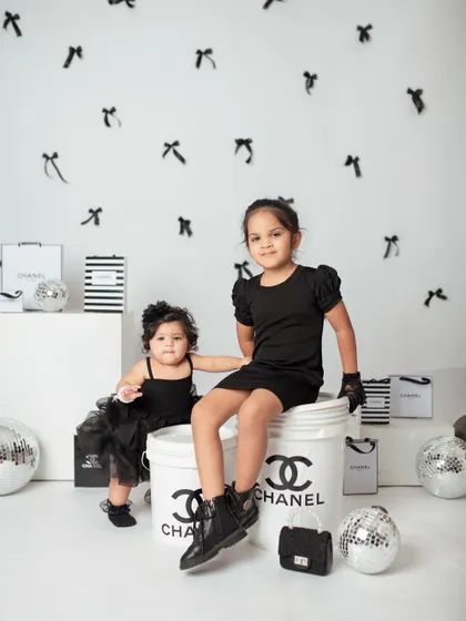 A full view of the sisters posing in their chic black outfits. The custom props and background really bring this creative theme to life.