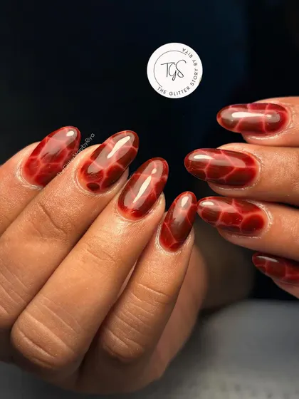 A unique and edgy tortoise shell or "tortie" nail design. This effect is created by layering sheer red and black polishes to get a deep, translucent pattern.