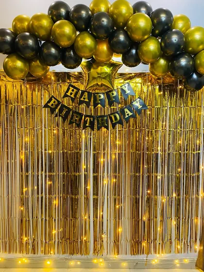 A classic birthday backdrop with a black and gold balloon arch over a golden foil curtain.