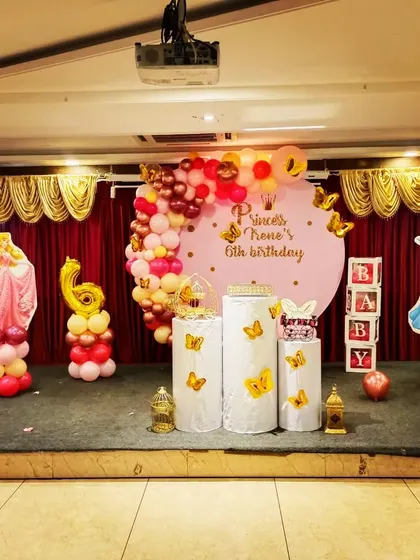 A simple and sweet princess theme for a 6th birthday party. The setup includes princess character cutouts, a round backdrop, and a pink and gold balloon garland.