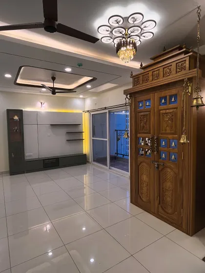 A picture-perfect view of a recently completed project. This living room features a contemporary TV unit that contrasts beautifully with a traditional, intricately carved wooden pooja unit, showing how we can blend different styles.