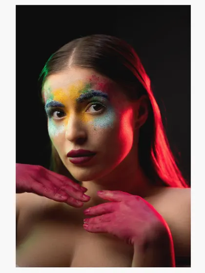 Another angle from the color-powder shoot, showing the model's hands covered in pigment. The contrast between the colorful makeup and the dark background is striking.