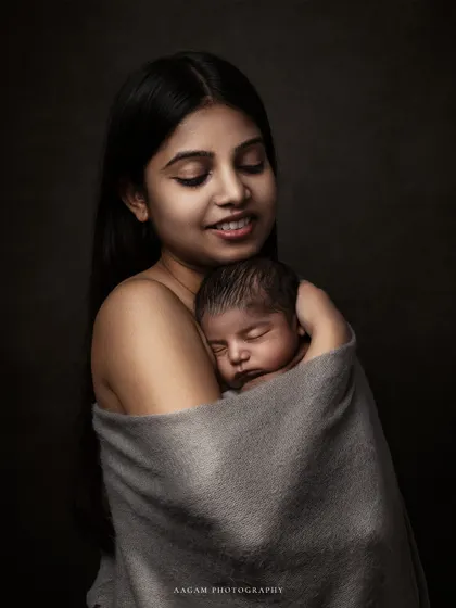 A mother's gentle embrace. This fine art portrait captures the serene and powerful bond between a mother and her sleeping newborn, wrapped together in a soft blanket.