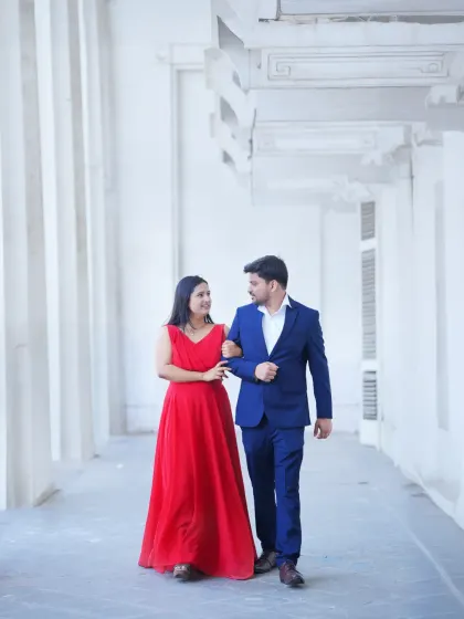 An elegant pre-wedding shot in a white colonnade corridor. The leading lines of the architecture create a beautiful composition, highlighting the couple in their formal attire.