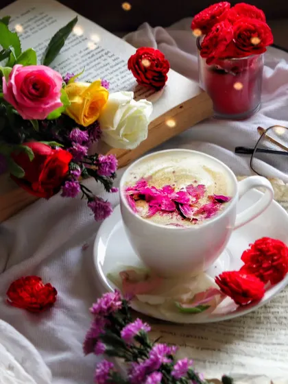 A beautiful flatlay of a coffee cup sprinkled with flower petals, surrounded by fresh roses and an open book. This shot is rich with detail and creates a romantic, literary mood.