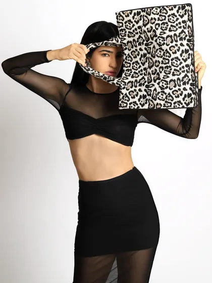 A bold and playful accessory shot. The model is styled in a sheer black top and skirt, creating a minimalist canvas to highlight the statement leopard-print tote bag.