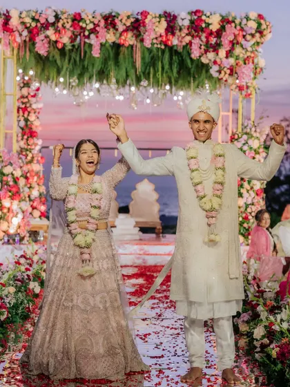 A moment of pure celebration as the couple raises their hands in joy after their sunset beach wedding ceremony.