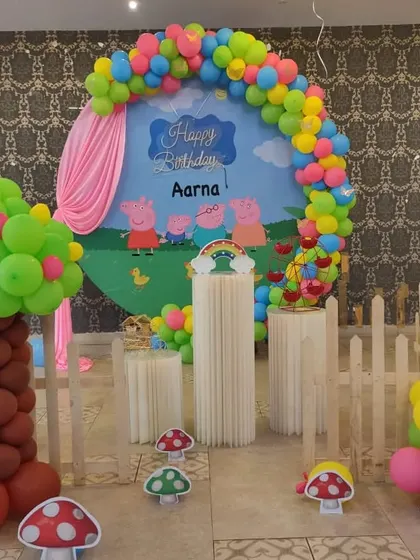 A playful Peppa Pig theme with a circular backdrop showing the whole family. The setup includes a balloon tree and mushroom props to recreate Peppa's world.