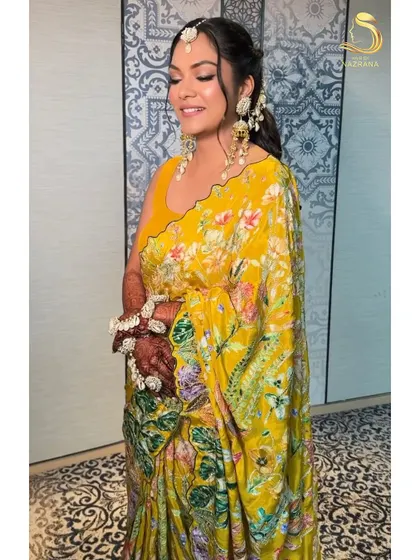 A happy bride showing off her personalized Haldi look, with her fiancé's name embroidered on her blouse and a stunning half-up hairstyle.